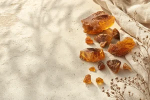 Uma natureza-morta editorial reúne fragmentos de resina âmbar natural sobre pedra calcária clara, com luz quente e espaço negativo.